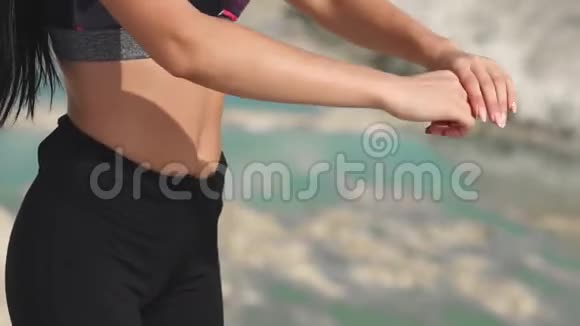 穿着黑色运动服的运动型黑发女孩在一个蓝水白垩沙场上训练在悬崖上做瑜伽视频的预览图