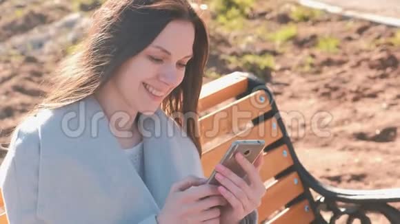 一幅快乐的黑发女人坐在公园的长凳上在手机上阅读和键入一条信息的肖像视频的预览图