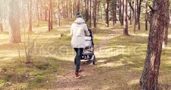 年轻的母亲带着婴儿车在森林里散步视频的预览图