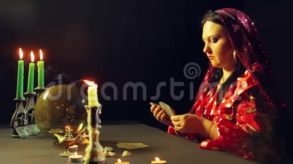 一个年轻的吉普赛人穿着红色的裙子在烛光下的桌子上读到了未来平均计划视频的预览图