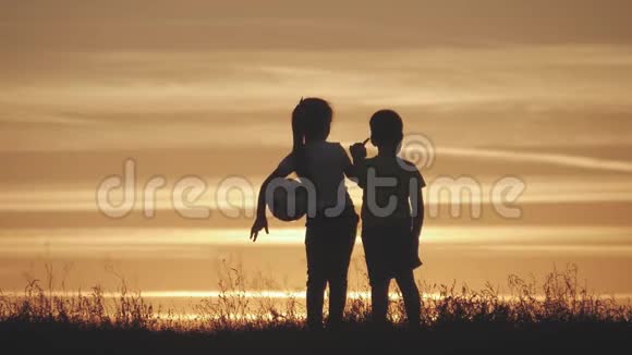 剪影两个快乐的孩子在草地上玩耍日落夏天视频的预览图