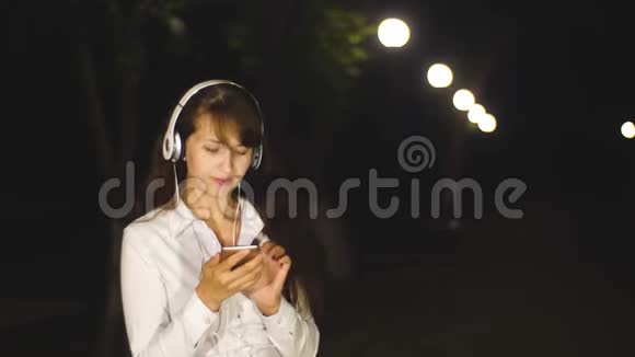 戴着耳机听歌唱歌的女人通过触摸电话在城市公园里唱歌视频的预览图