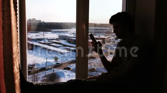 一个拿着手机坐在窗台上的男人的剪影视频的预览图