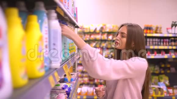 女人在商店里选择家用化学品女人在超市选择柔软剂视频的预览图
