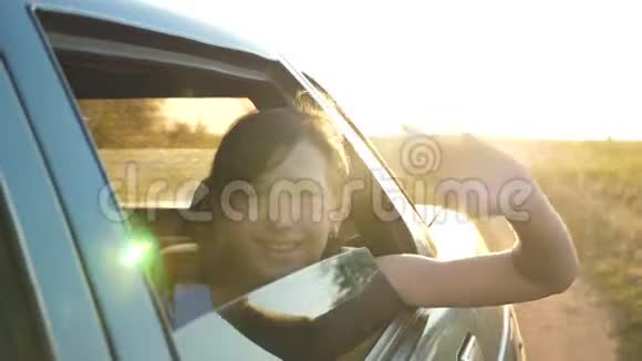 美丽的女孩坐在车里双手放在窗前微笑着在明亮的灯光下挥动着她的手视频的预览图