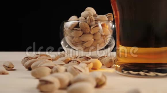 新鲜啤酒啤酒杯中的美味啤酒靠近开心果碟放入黑色背景的木桌中新鲜的视频的预览图