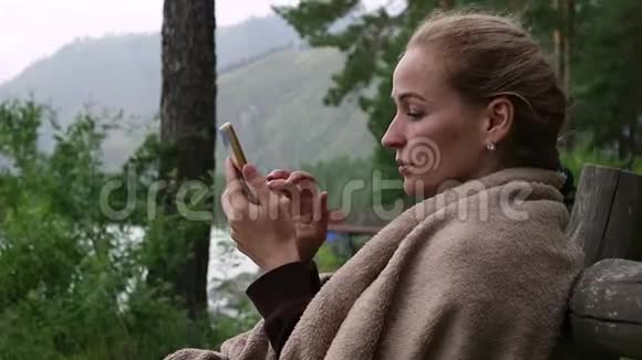 年轻女子在靠近山河的公园长椅上放松用智能手机发送信息视频的预览图