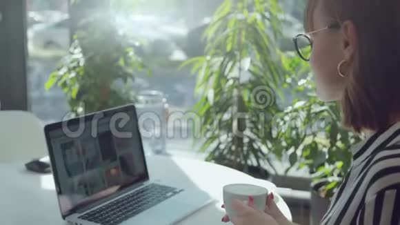 有笔记本电脑的咖啡馆里的女孩正在喝咖啡她又回到了镜头前视频的预览图