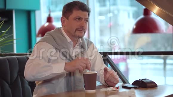 一个穿着白色衬衫的男人穿着毛衣用棍子在刚做的早晨咖啡里搅拌糖视频的预览图