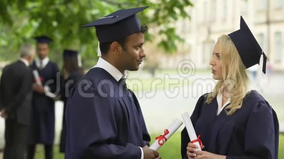 戴着毕业证书的戴着学术服装和帽子的人在手里交谈毕业日视频的预览图