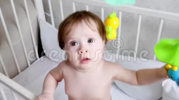 一个尿布上的小婴儿第一颗乳牙站在婴儿床上他的玩具和游戏视频的预览图