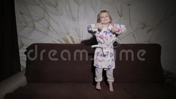 金发可爱的小女孩跳上沙发浴衣快乐视频的预览图