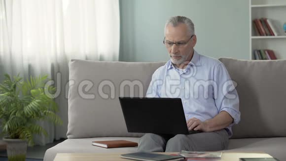 50岁的男性坐在沙发上在笔记本电脑上工作自由职业者和职业视频的预览图