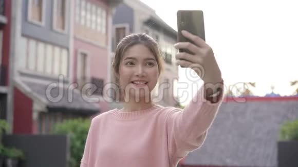 开朗美丽的年轻亚洲背包客博主女士在唐人街旅行时使用智能手机自拍视频的预览图