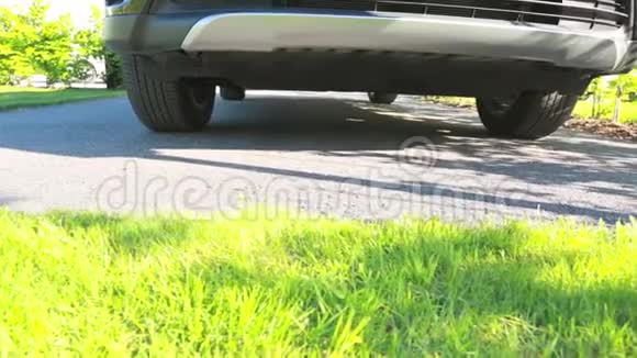 在一辆停在沥青停车场的汽车下缓缓移动视线它周围有绿草和绿色植物视频的预览图
