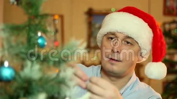 一个戴着圣诞老人帽子的年轻人在hous装饰一棵圣诞树视频的预览图
