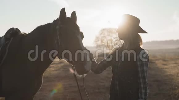 年轻的金发女孩戴着牛仔帽抚摸和拥抱马享受大自然视频的预览图