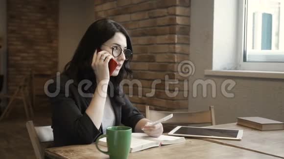 戴眼镜的时髦女人坐在办公室的桌子旁打电话视频的预览图