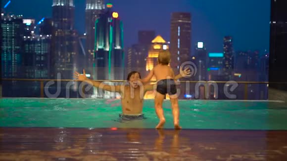 一个年轻人和他的小儿子在屋顶的游泳池里玩得很开心看到了摩天大楼视频的预览图