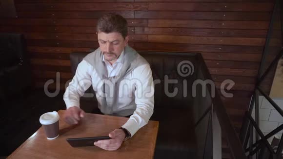 成年帅哥在一家咖啡馆里工作在平板电脑上喝咖啡视频的预览图