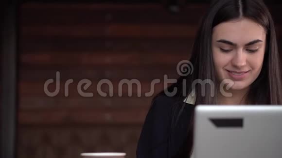 可爱的黑发女孩在笔记本电脑上工作喝咖啡视频的预览图