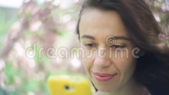 年轻的微笑美丽的旅游妇女带着电话在春暖花开的公园放松视频的预览图