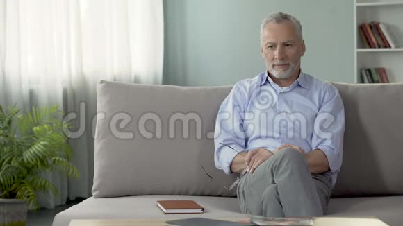 健康的老人坐在沙发上戴着眼镜梦想着度假视频的预览图