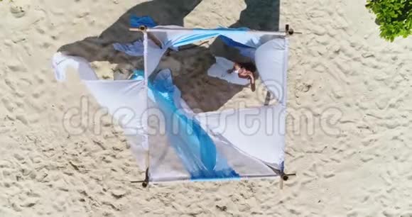 空中美丽的女孩在白色沙滩上的婚礼拱门上摆姿势视频的预览图