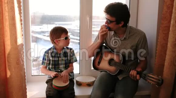 戴着太阳镜演奏乐器爸爸在弹吉他儿子坐在窗台上打鼓视频的预览图