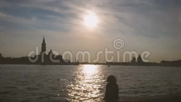 一个女孩坐在威尼斯运河里享受日落的剪影视频的预览图