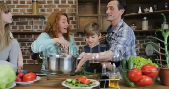 快乐的家庭忙碌的烹饪美味晚餐父母和两个孩子在厨房交谈同时准备食物视频的预览图