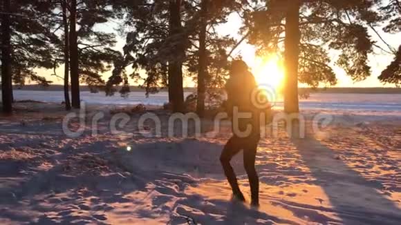 一个年轻的白种人女孩背着背包在冬天的森林道路上在日落时覆盖着冬天的松林步行视频的预览图