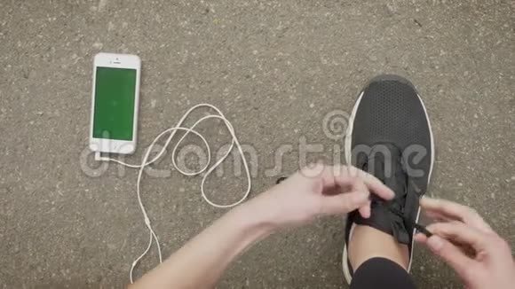 女运动员系着鞋带而她的智能手机和耳机则躺在地上彩色屏幕通讯视频的预览图