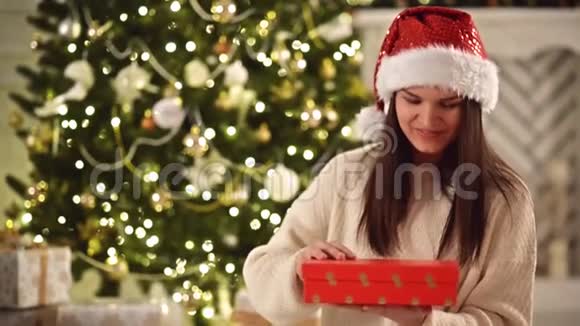 圣诞帽里的年轻漂亮女孩打开圣诞礼物然后微笑笑得惊魂未定的女人视频的预览图