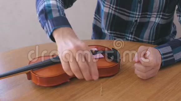 穿格子衬衫的年轻人的特写双手正在修理坐在桌子旁的小提琴拧紧螺栓就位视频的预览图