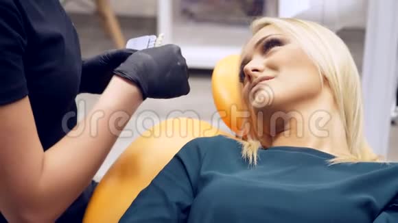 一位坐在牙医A椅子上的女性病人等待牙医A助手确定她牙齿的阴影颜色视频的预览图