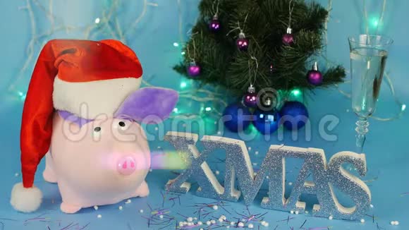 软玩具粉红色的猪戴着红色圣诞老人帽子背景是一棵蓝色的圣诞树一杯视频的预览图