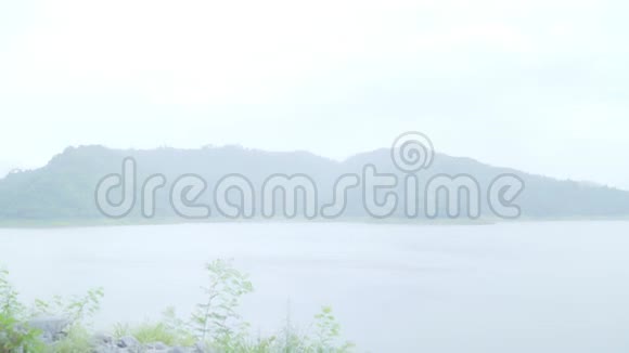 年轻的亚洲甜蜜的一对夫妇感到快乐用浪漫的时间打雨穿着雨衣站在湖边视频的预览图