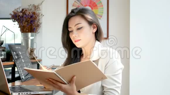 4K镜头美丽的亚洲商务女性坐在电脑手提电脑键控数据阅读和翻页笔记簿页面视频的预览图