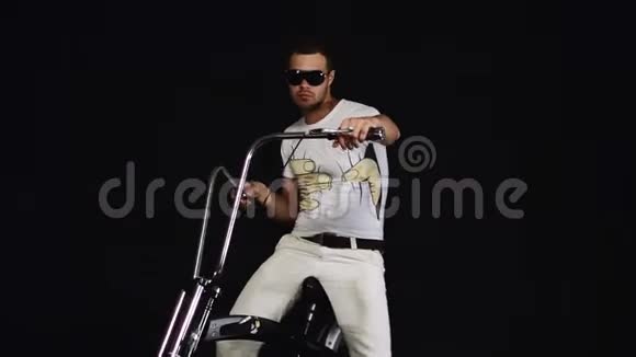 戴墨镜的帅哥坐在黑色自行车上向后移动视频的预览图