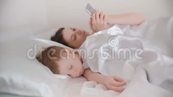 妈妈醒来在她的儿子还在睡觉的时候用手机浏览互联网视频的预览图