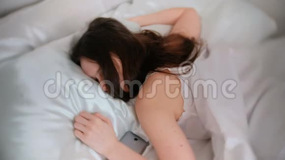 睡在床上的黑发女青年手机靠近她视频的预览图