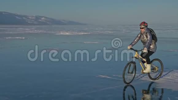 女人在冰上骑自行车女孩穿着银色的羽绒服背包和头盔骑自行车的人视频的预览图