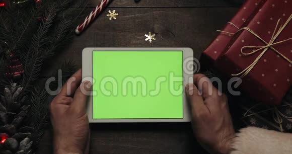 圣诞老人手里拿着绿色屏幕的白色平板电脑另一只手把一些礼物盒放在视频的预览图