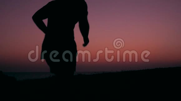 年轻快乐的男人在美丽的粉红夕阳下奔跑跳跃的剪影HD慢速运动免费生活方式自由视频的预览图
