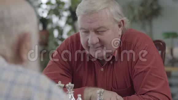 成人朋友下棋坐在家里的皮革沙发上大胡子的人在想哪个棋子要动一动视频的预览图