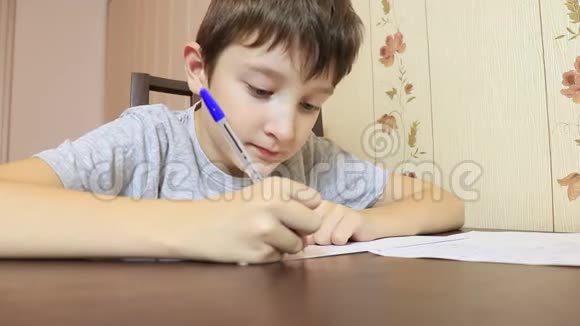 一个男孩坐在家里的桌子旁用钢笔在纸上写字视频的预览图