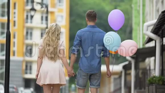 一对夫妇牵着手走在街上停下来亲吻拿着气球的家伙视频的预览图