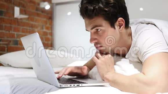 躺在床上的年轻人在笔记本电脑上工作并对成功作出反应视频的预览图