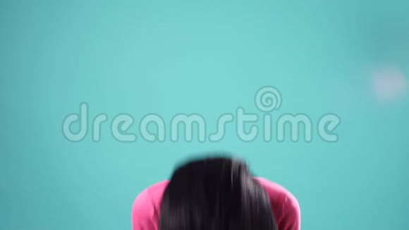 微笑的黑发女人玩弄她的头发看着镜头上的绿松石背景视频的预览图